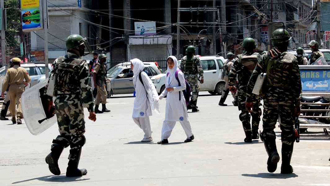 IN SHOCK: College students pass by the security forces to their homes after classes were suspended in educational institutions as a precautionary measure following the killing of Hizbul Mujahideen commander Sabzar Bhat in an encounter in Pulwama, UNI