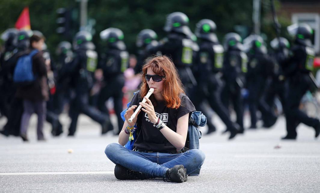 OTHER VOICES: A protestor plays the flute as German police walk behind at a demonstration during the G20 summit in Hamburg, Germany, Reuters/UNI