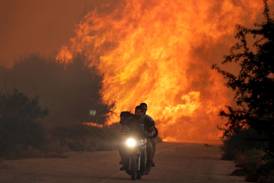NATURE STRIKES BACK: Two men and a dog on a motorbike flee a wildfire burning near the village of Varnavas, north of Athens, Greece, Reuters/UNI