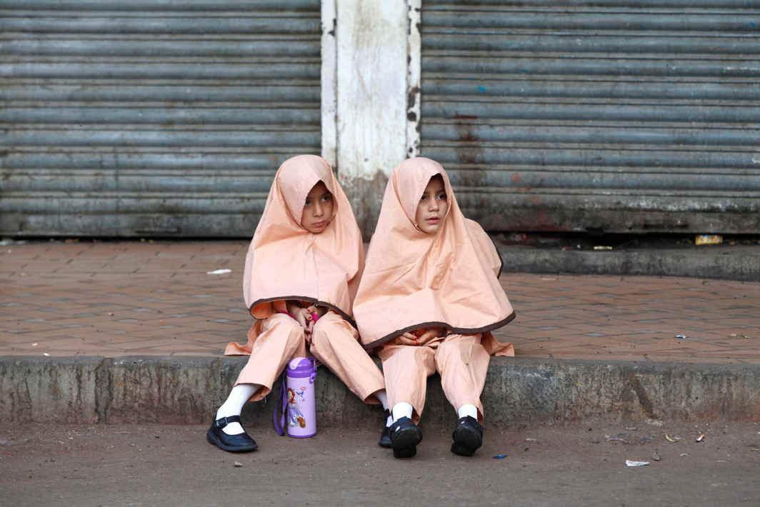 LIMITED CHOICES: Girls in uniform sit along a sidewalk while waiting for school van in Karachi, Pakistan, Reuters/UNI